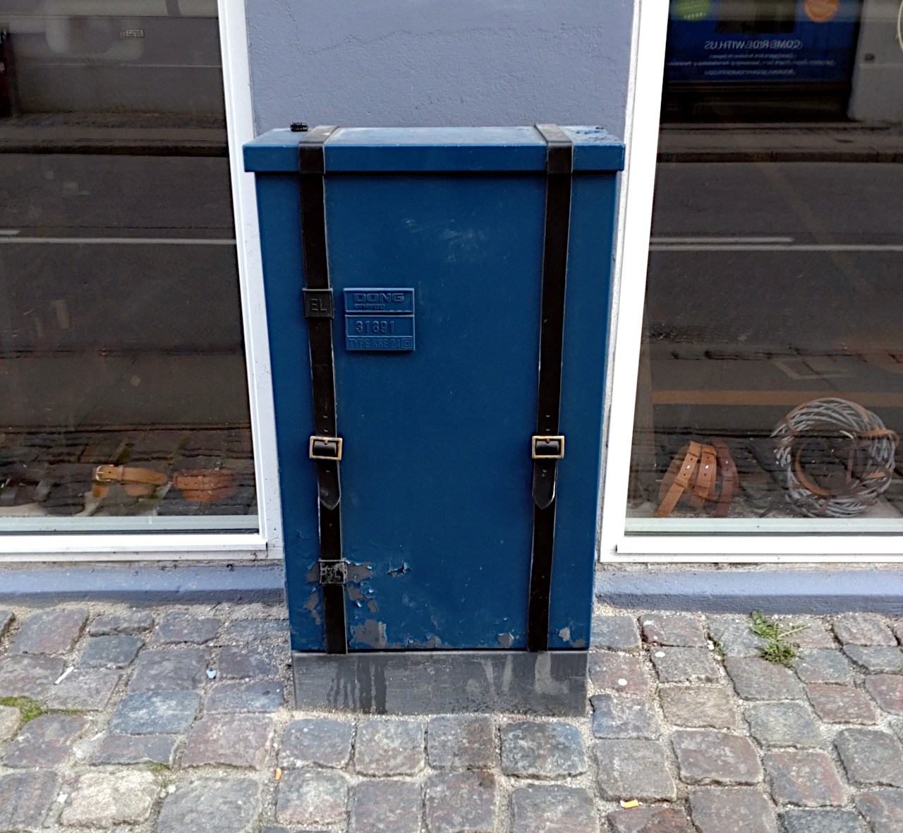 Eletrical cabinet in the street, painted blue and with a set of leather suspenders mounted.